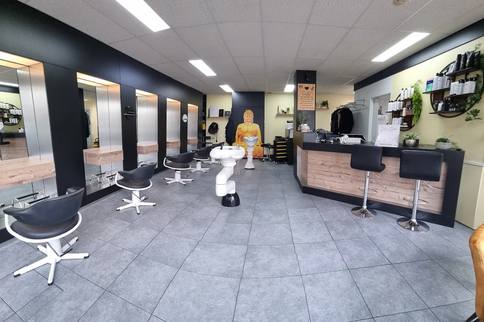 De salon van binnen: spiegelwand met zwarte panelen, houten balie en achterin de gouden boeddha