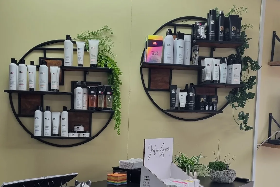 De twee ronde zwarte wandrekken met planten en KIS-producten aan de olijfgroene muur, de houten balie ervoor